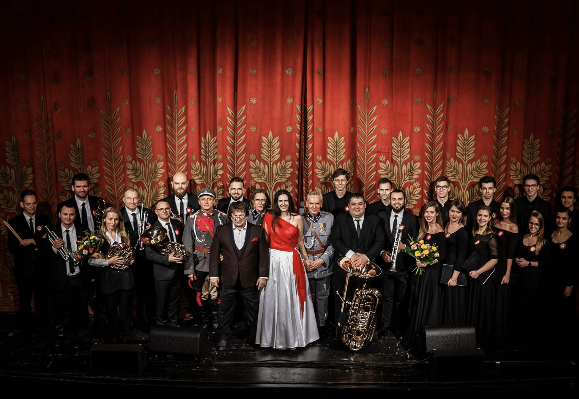 Yasmina w centrum sceny, w bieli i czerwieni, z orkiestrą, chórem i solistami na tle czerwonej kurtyny teatralnej